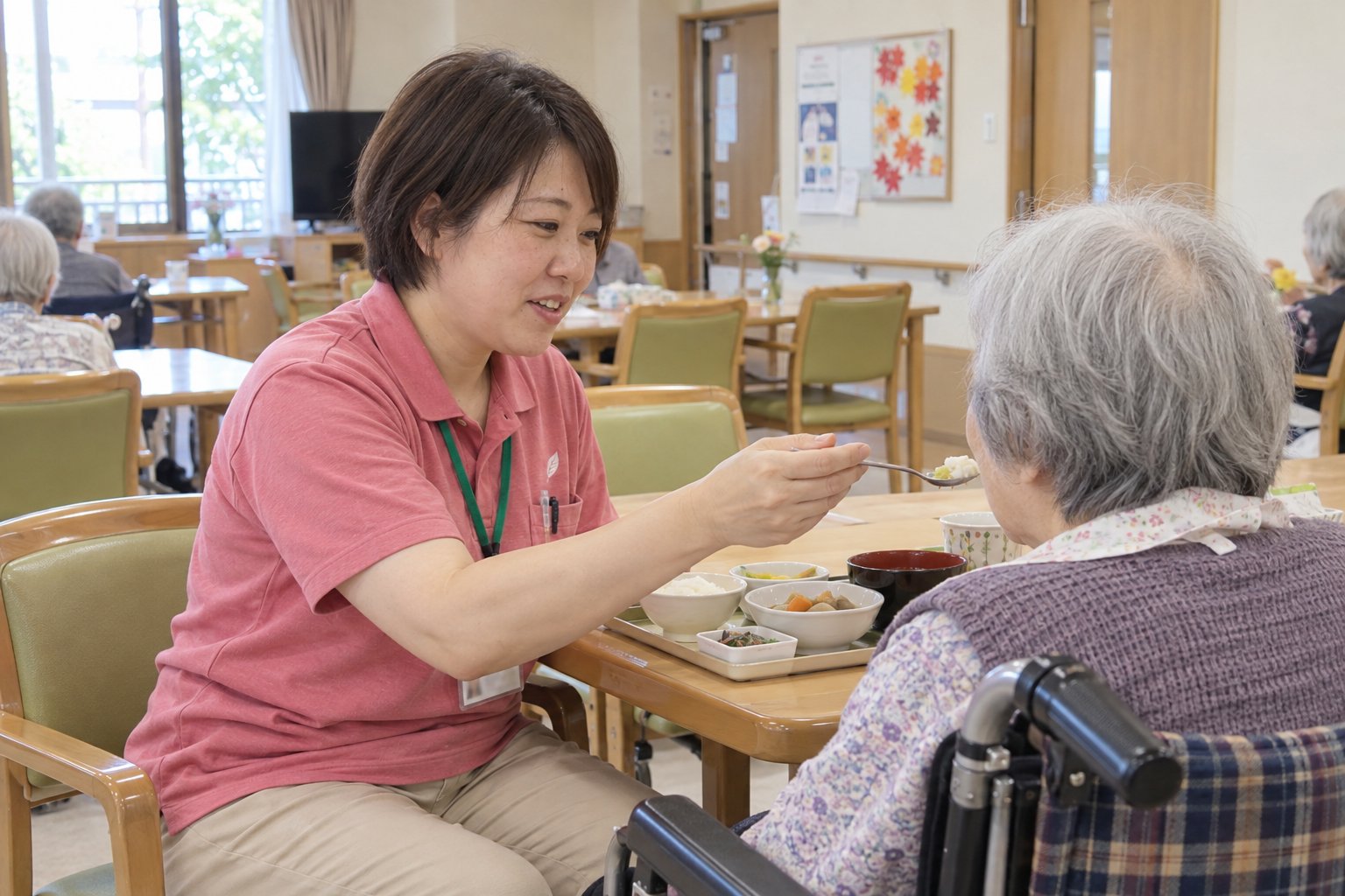 食堂で、職員が車いすのご入居者の食事を手伝っている